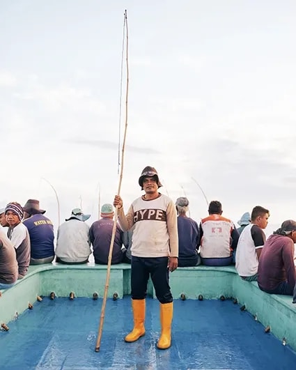 Visser op de boot in Bitung met hengel in zijn hand en gele kaplaarzen aan. 