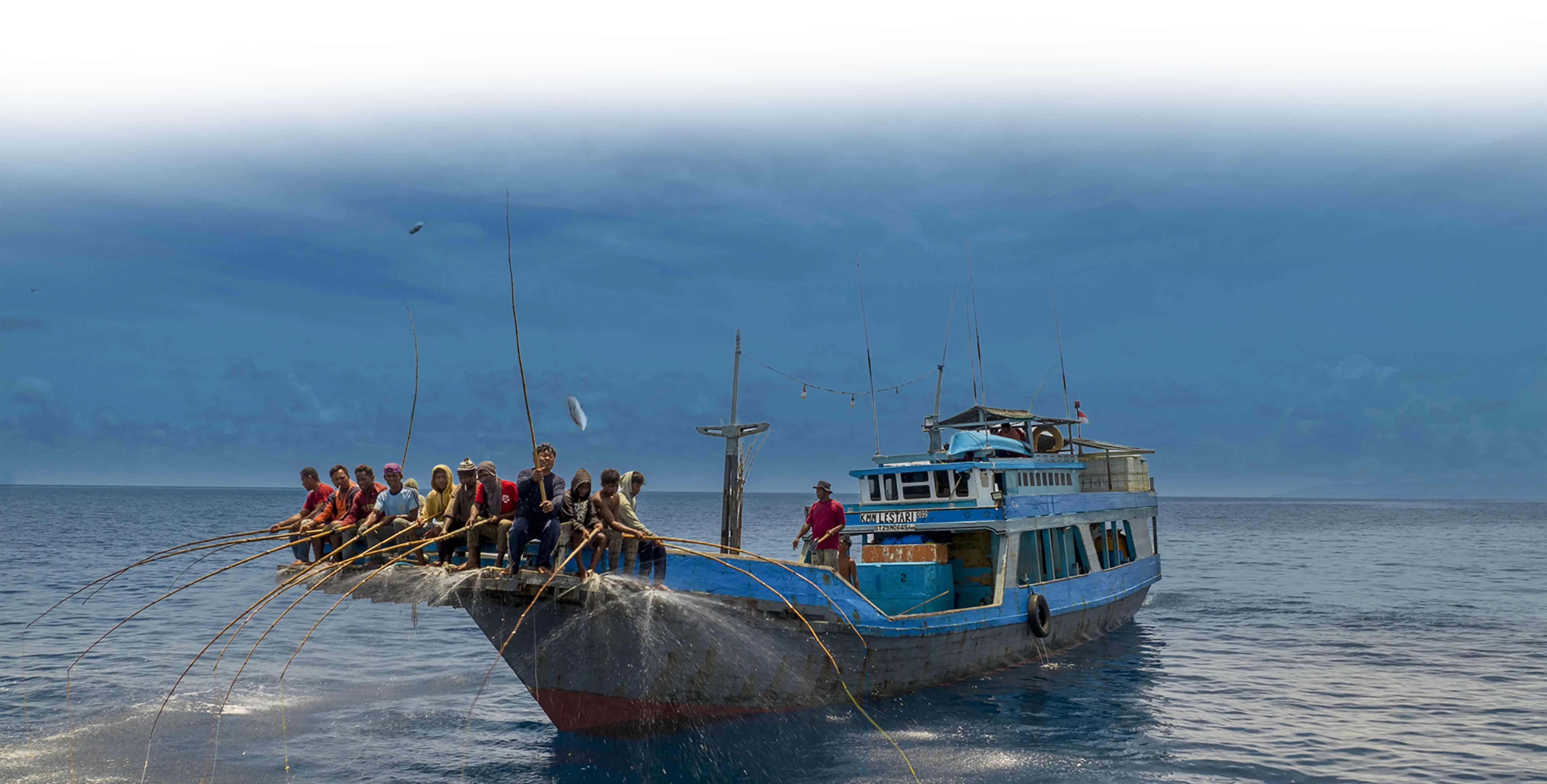 A blue fishing boat with many people on deck pulling nets in the open sea.